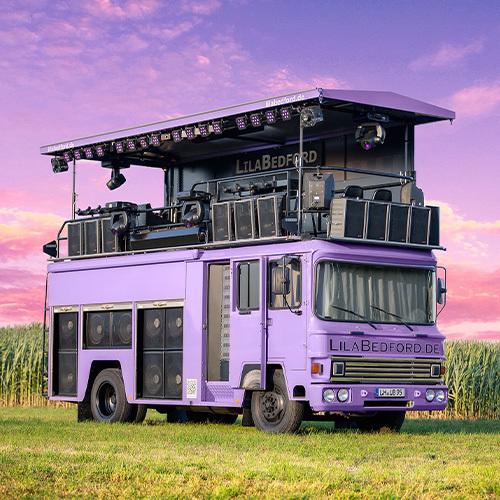 Antenne Münster Partytruck Ein lilafarbener Bus. Obendrauf ist eine Bühne mit vielen Musikboxen und Scheinwerfern