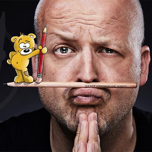 Karikaturist Preisselbär Ein Mann balanciert einen Bleistift auf der Oberlippe. Am Ende des Bleistiftes ist eine Zeichnung eines kleinen Comic-Bären, der einen roten Bleistift in der Hand hat