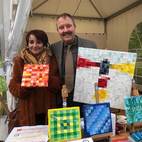 Quadratologo Ein Mann und eine Frau halten Bilder hoch, die aus kleinen Einzelquadraten bestehen.
