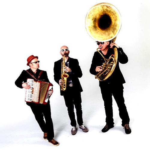 Walking Band drei schwarz gekleidete Männer mit Sonnenbrillen. Einer spielt Tuba, einer Saxophon und einer Akkordeon
