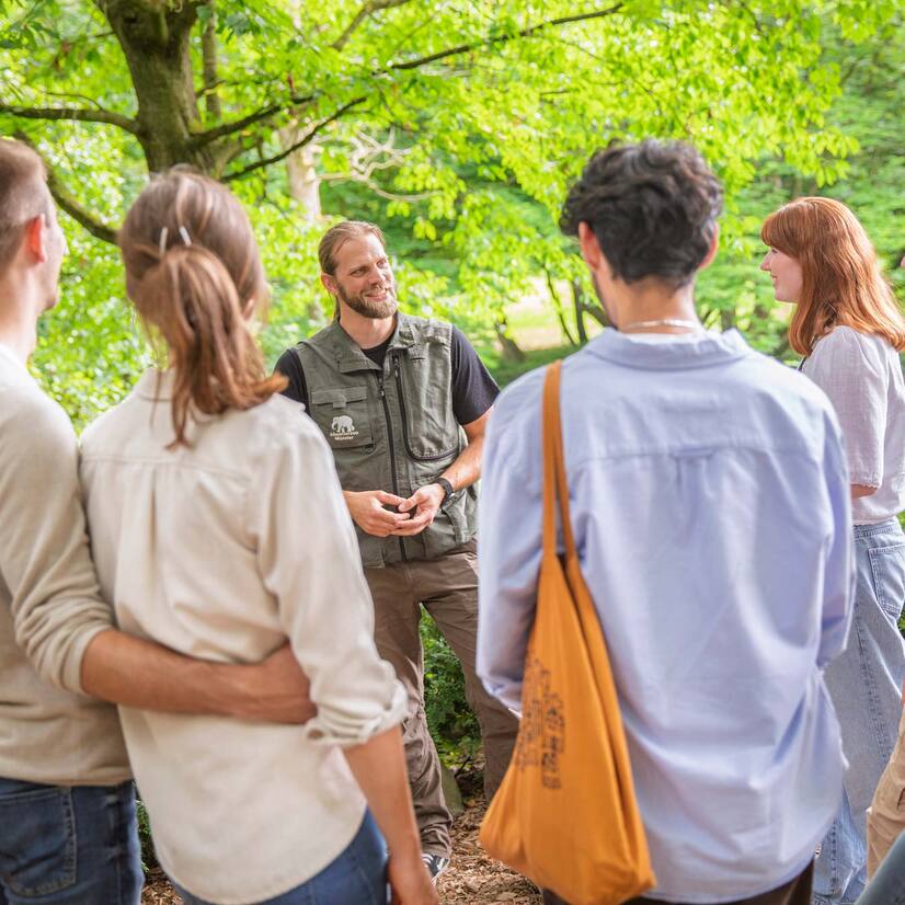Eine Gruppe Menschen steht vor einem Mann mit Zoo-Weste und h&ouml;ren gebannt zu