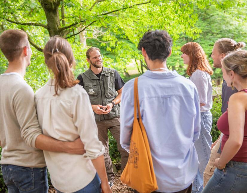 Gruppe mit Pfleger Eine Gruppe Menschen steht vor einem Mann mit Zoo-Weste und hören gebannt zu