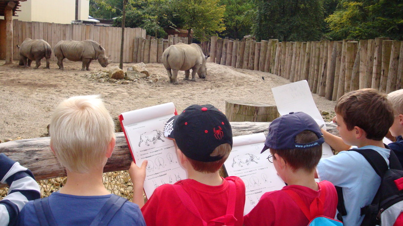 Kinder in der Zooschule mit Unterrichtsmaterial vor dem Nashorngehege