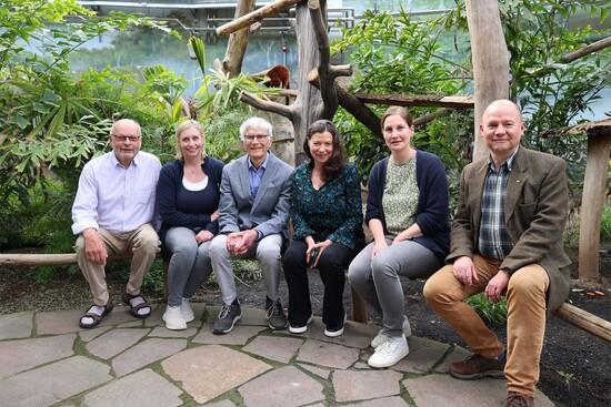 Die Leitung des Allwetterzoos, des Zoovereins und des Pferdemuseums sitzt auf einem Geländer vorm Gehege der Roten Varis