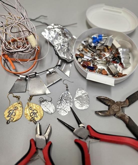 Schmuckwerkstatt Ohrringe aus Metallblech, die scheinbar aus Altmetall und Schrott hergestellt wurden. Unten liegen Zangen und Seitenschneider.